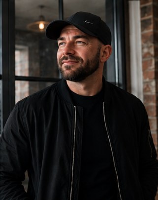 Kameron Frisby by a window in a cap and bomber jacket